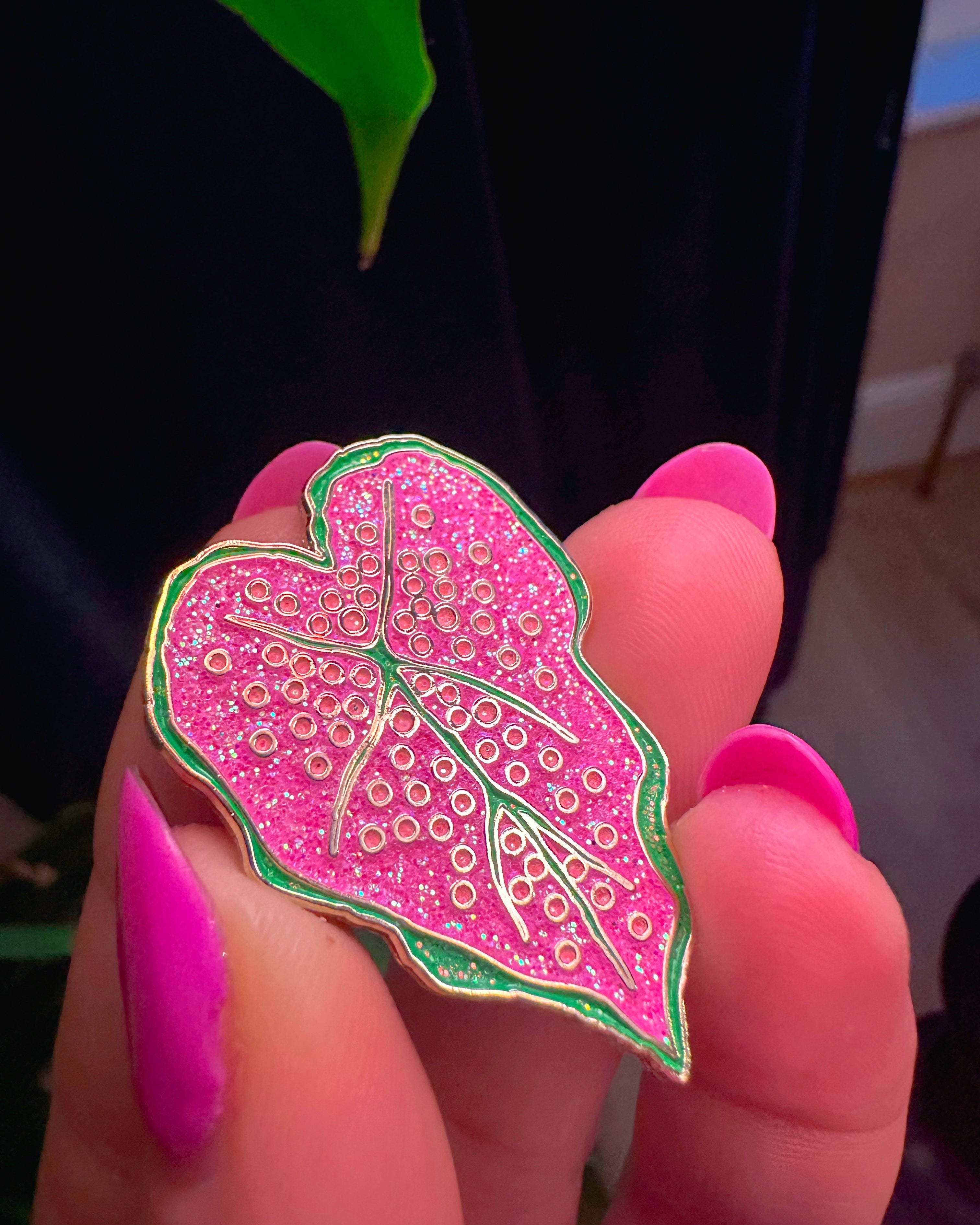 Pink leaf-shaped pin held between fingers with a blurred background
