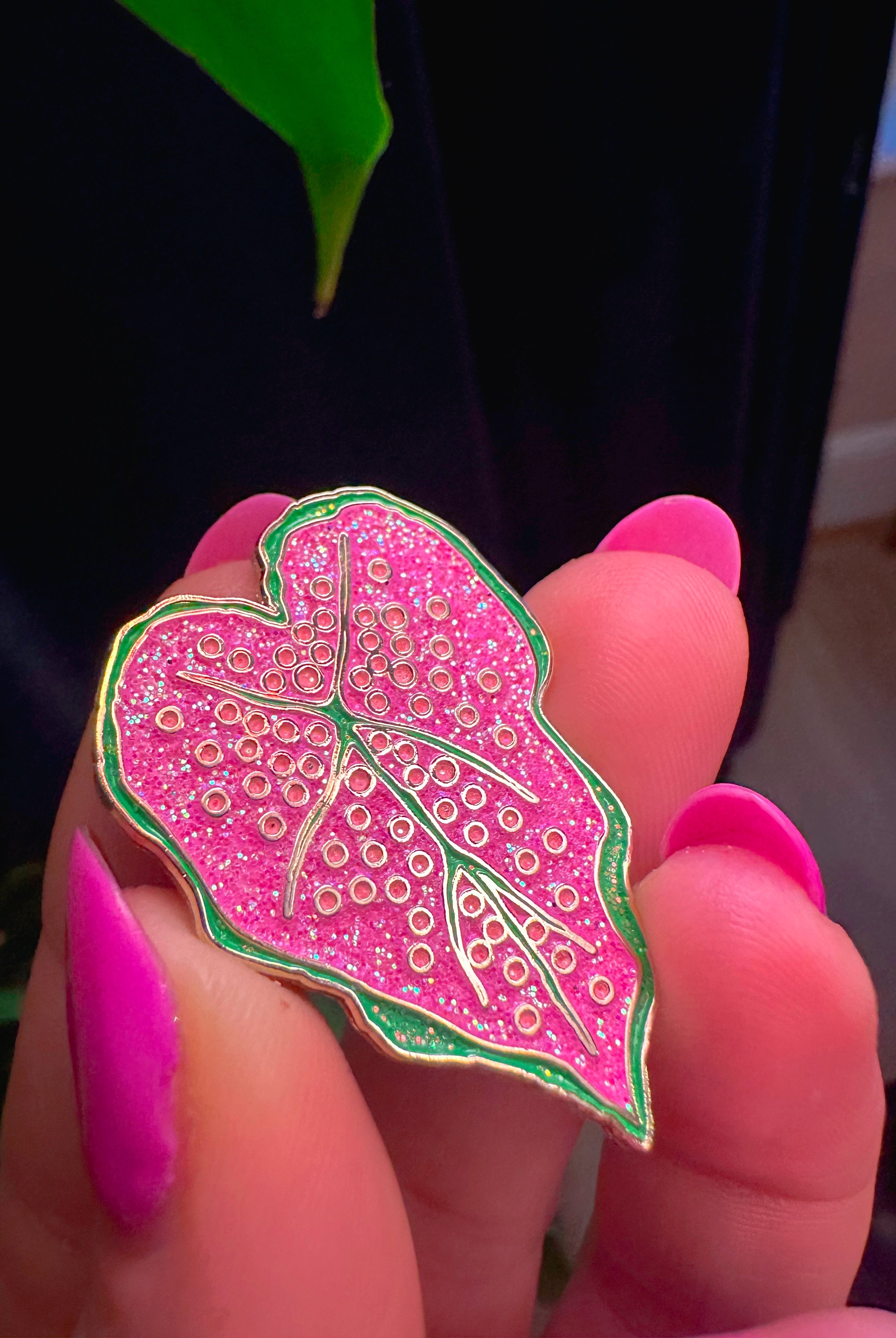 Pink leaf-shaped pin held between fingers with a blurred background