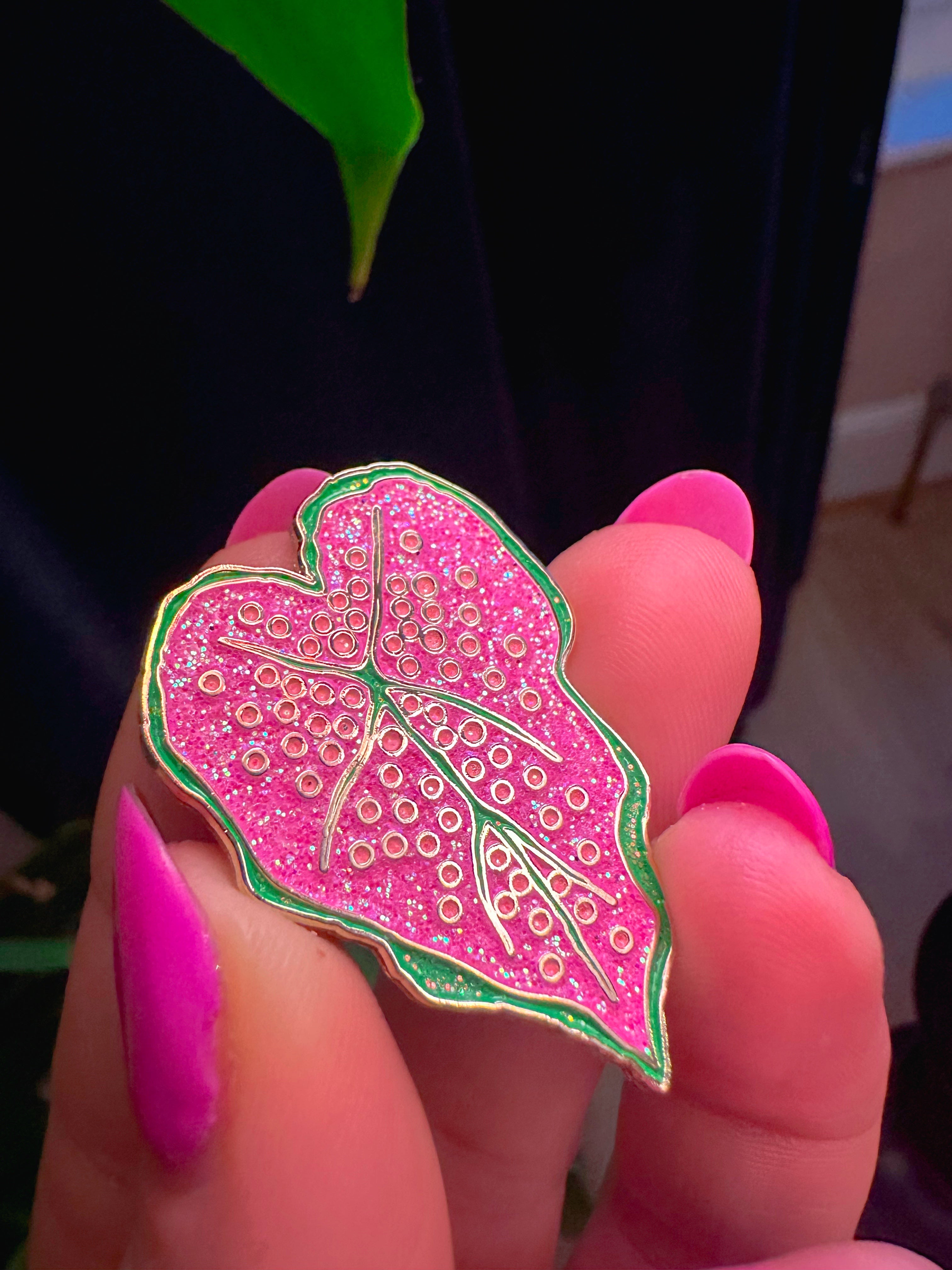 Pink leaf-shaped pin held between fingers with a blurred background