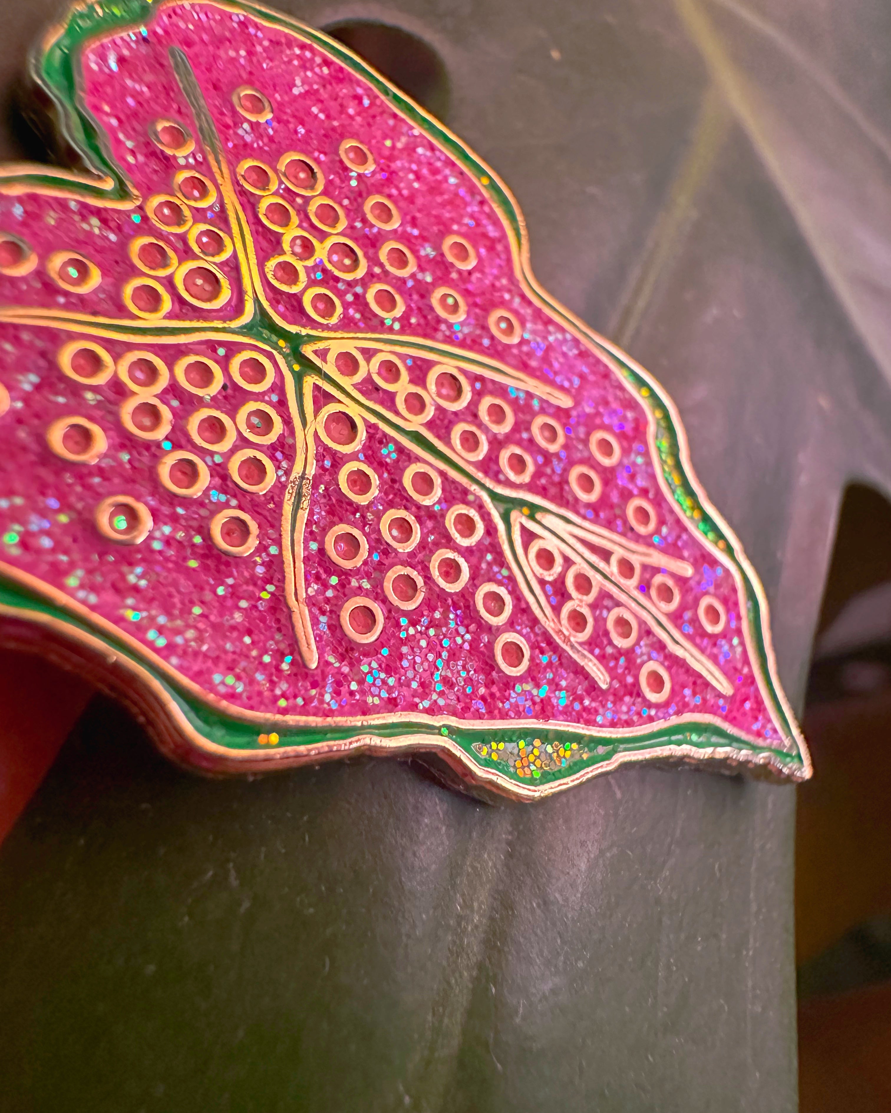 Decorative pink leaf-shaped object with gold patterns on a gray background