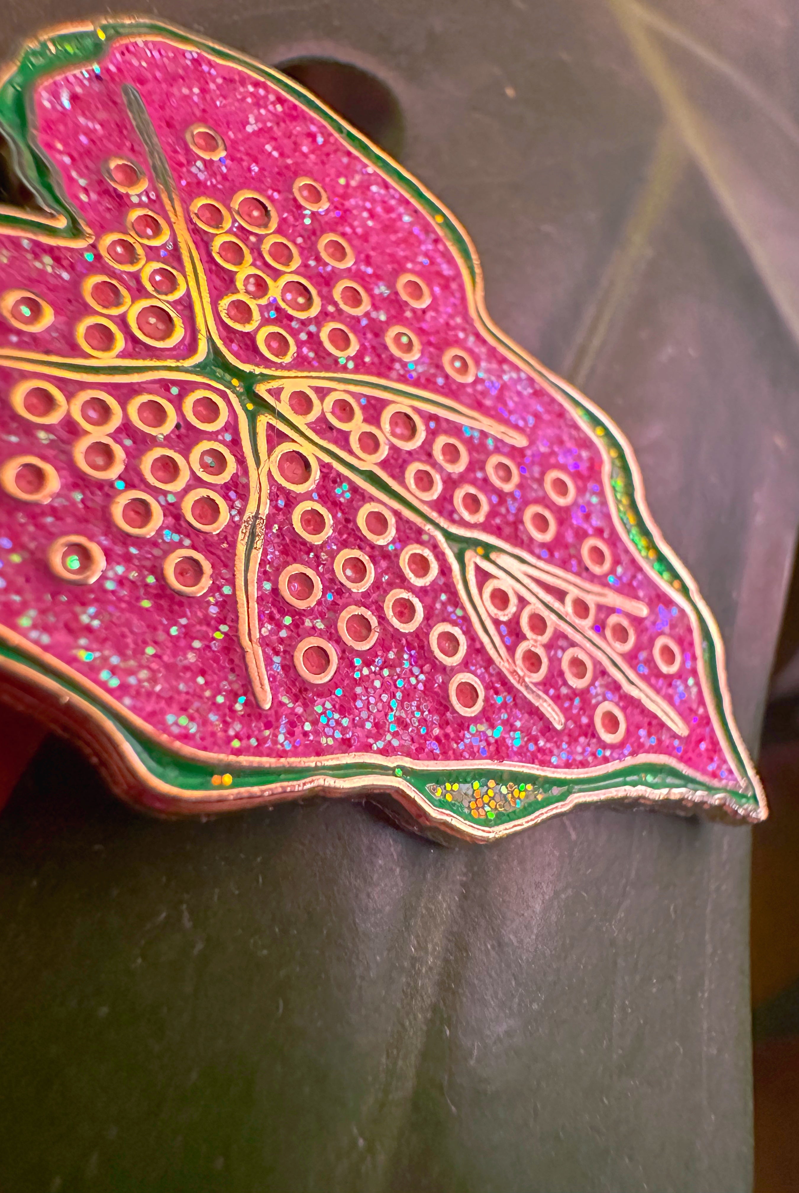 Decorative pink leaf-shaped object with gold patterns on a gray background