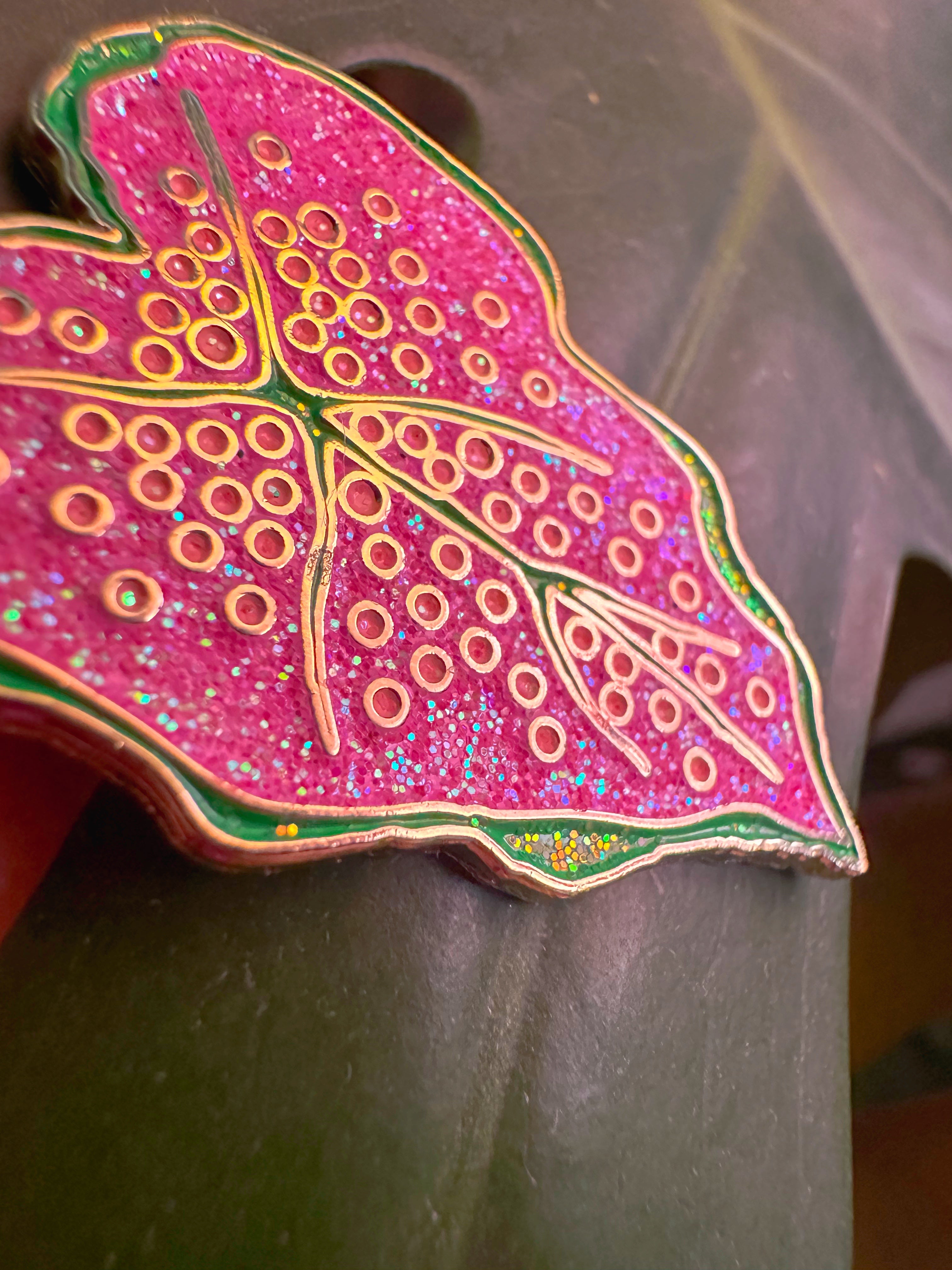 Decorative pink leaf-shaped object with gold patterns on a gray background