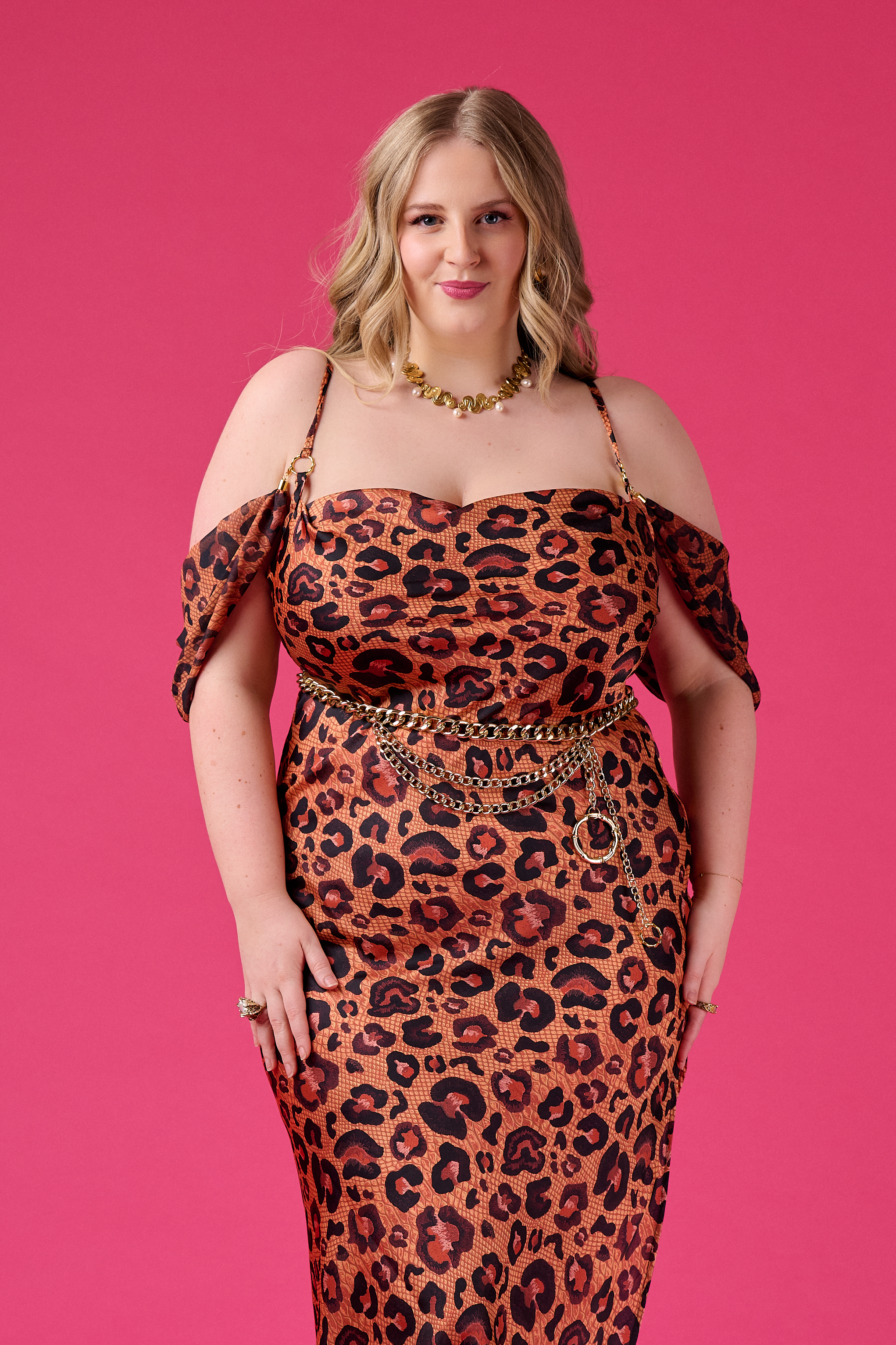 Woman wearing a leopard print dress with gold accessories on a pink background