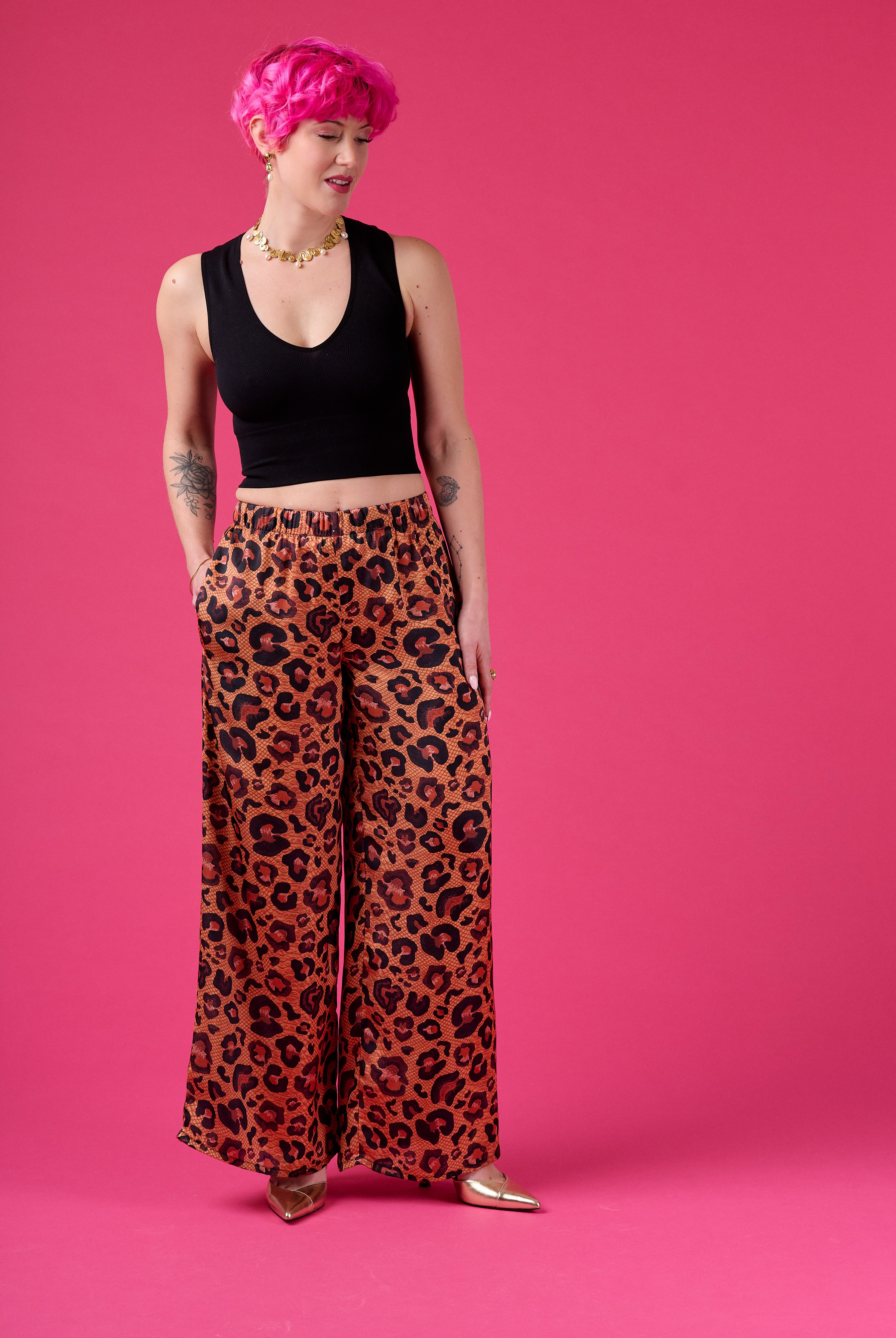 Person wearing a black top and leopard print pants on a pink background