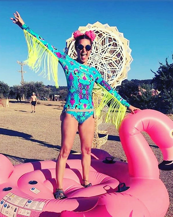 modeal at festival on inflatable flamingo wearing neon fringed turquoise blue and purple lycra bodysuit