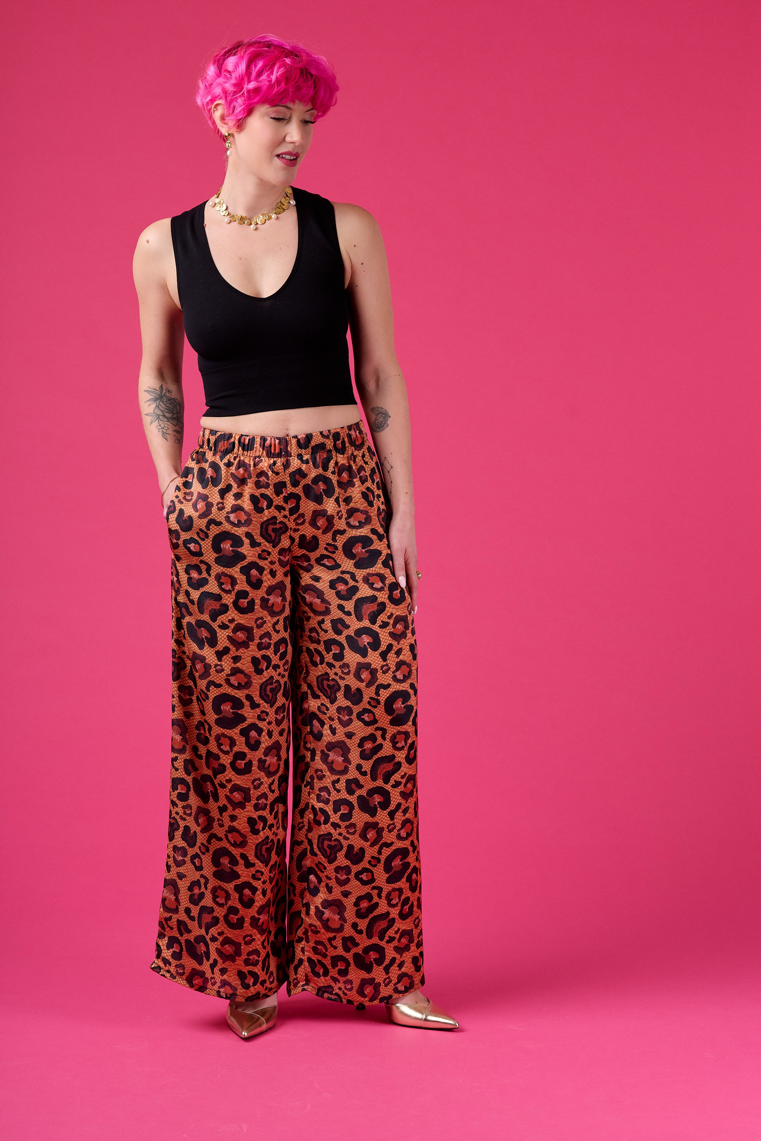 Person wearing a black top and leopard print pants on a pink background